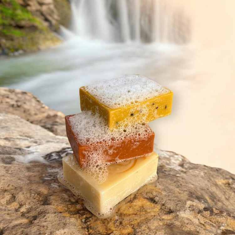 3 savons corps Mel'Uniq avec leur mousse sur fond de cascade naturelle
