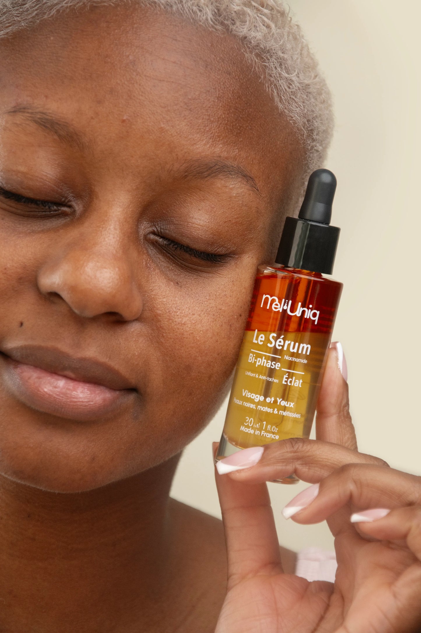 Femme à la peau noire tenant le sérum bi-phase éclat Mel’Uniq visage et yeux